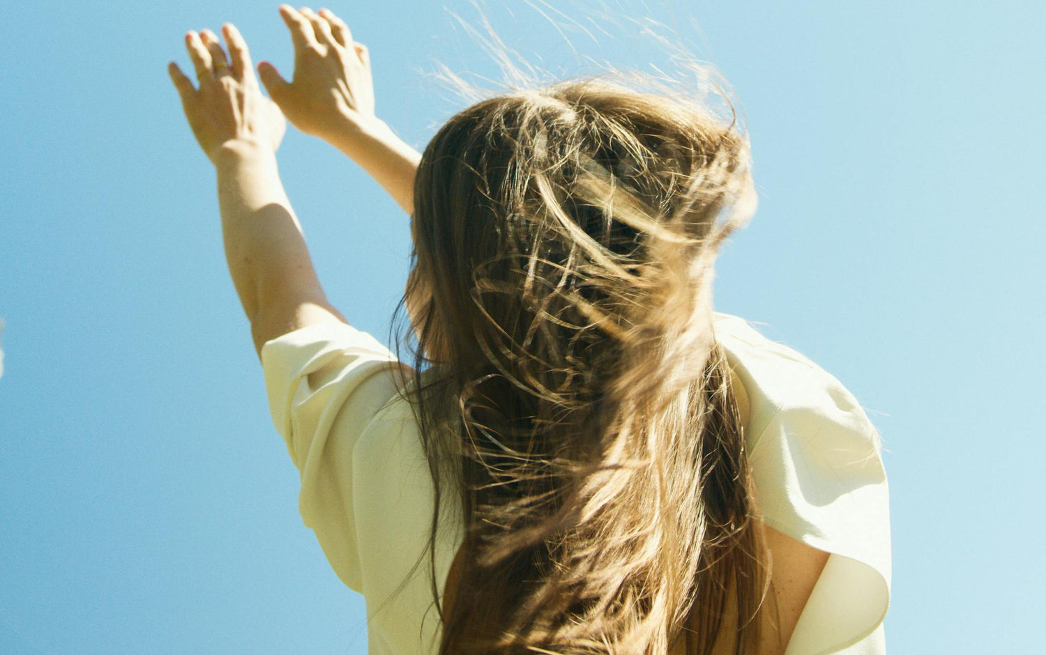 Person with long hair and arms raised against a clear blue sky